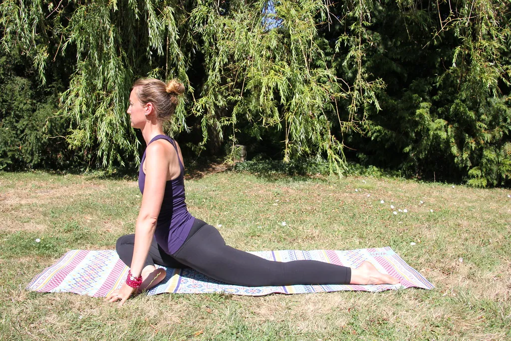 Woman in pigeon pose on a mat outdoors