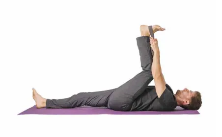 Man lying on his back pulling one leg up with a strap