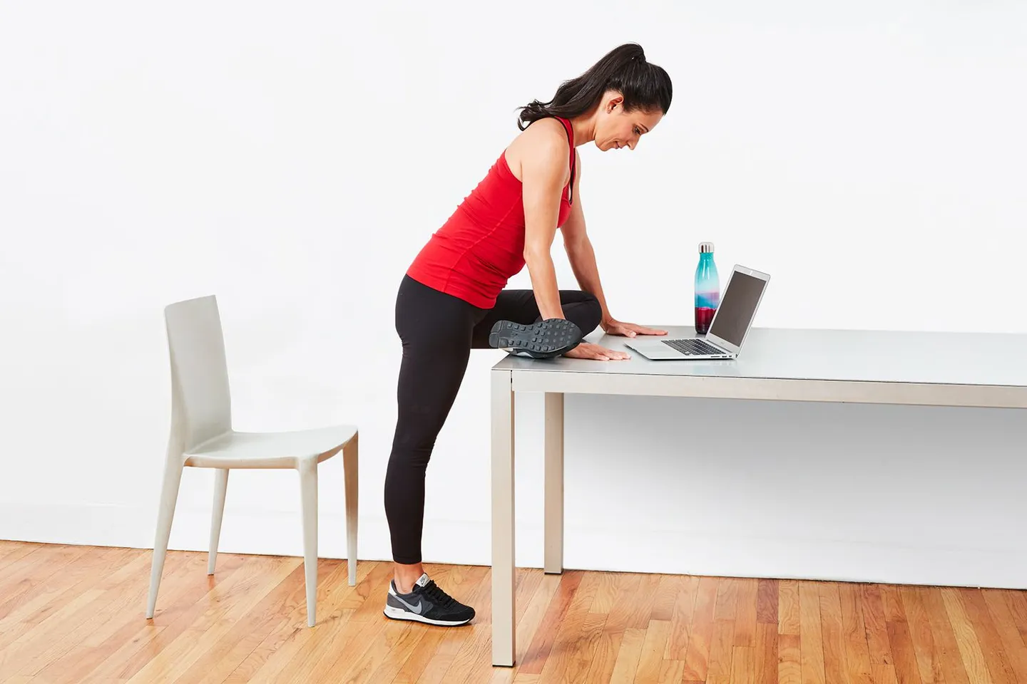 Woman doing a standing pigeon stretch with her leg on a table