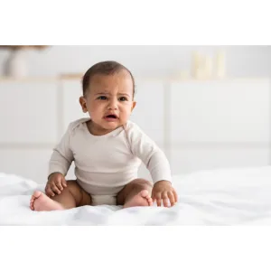 Crying baby sitting on a bed